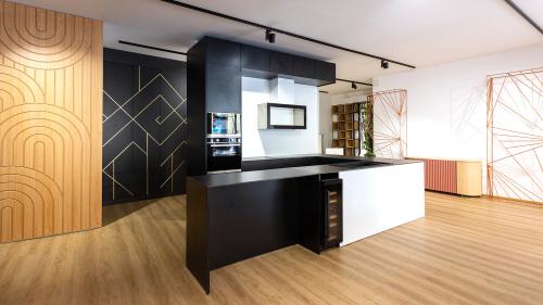 The focal point of the space is a bespoke black-and-white kitchen, combining minimalist aesthetics with outstanding functionality. Its clean lines and carefully selected materials create an elegant and timeless appearance.  Behind the kitchen, a custom-built cabinet features distinctive gold decorative inlays. The refined geometric metallic pattern adds a luxurious visual accent, enhancing the sophisticated character of the interior.